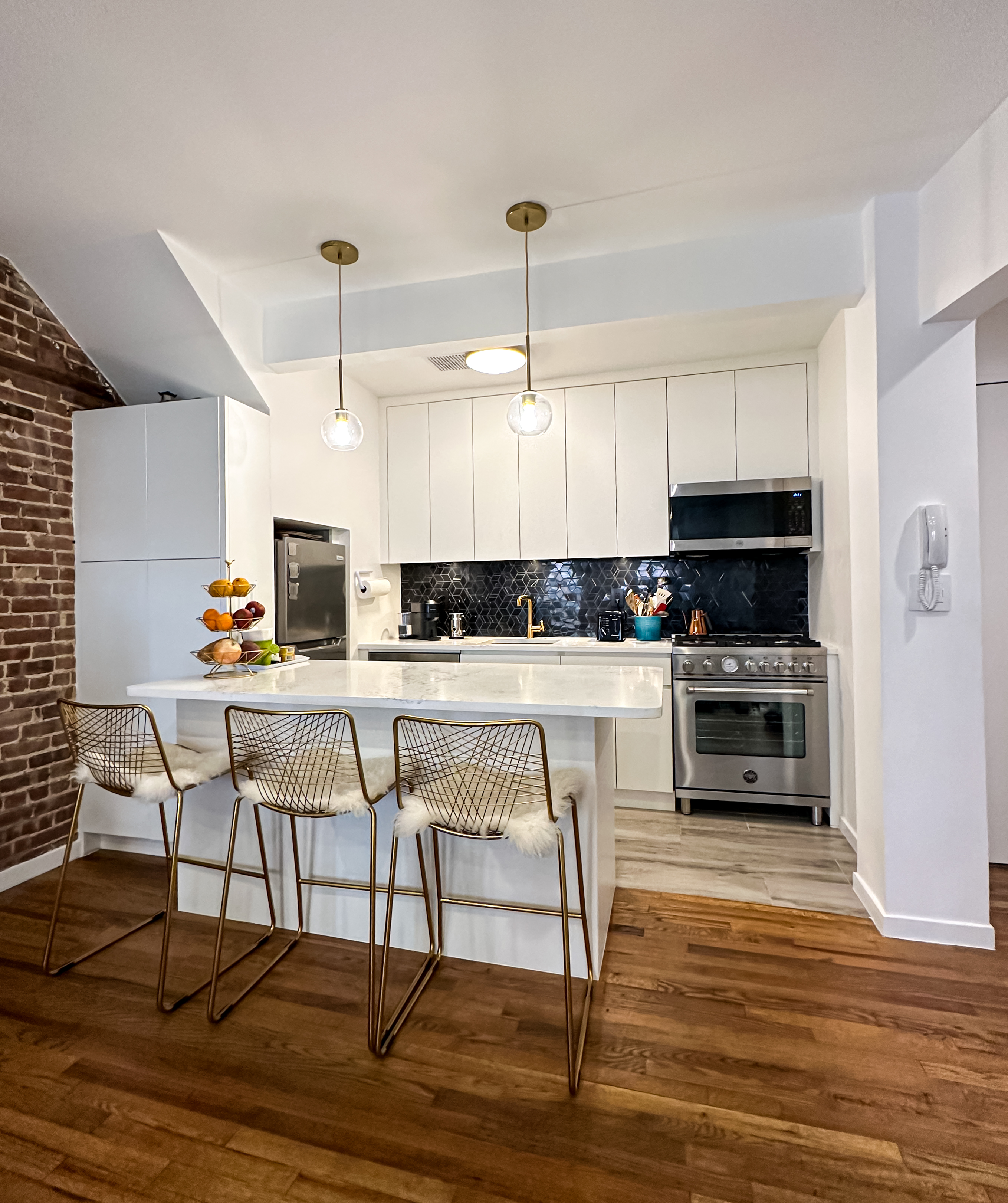 Kitchen — black geometric tile, brass pendants, marble island, exposed brick